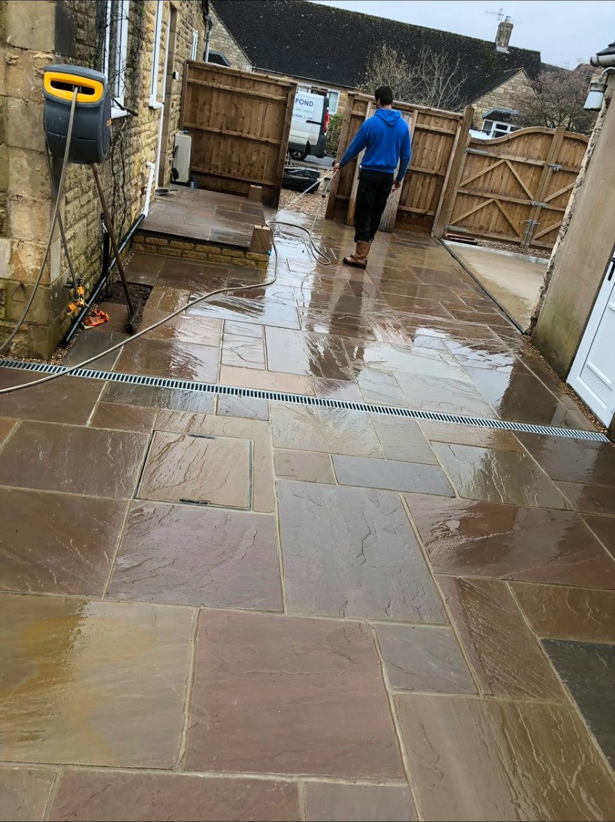 Riven natural stone patio with integrated drainage channel and timber fencing.