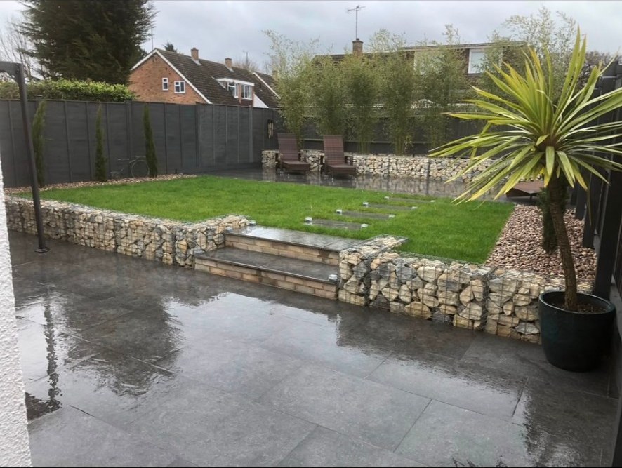 Contemporary garden with grey porcelain patio, gabion stone walls, lawn and bamboo screening.
