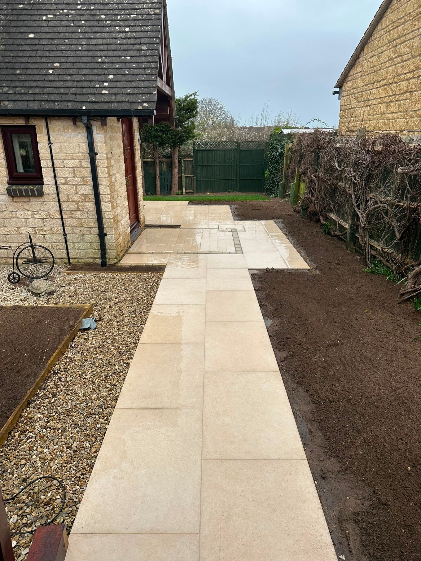 Contemporary beige porcelain garden path and patio with fresh topsoil borders and gravel area.