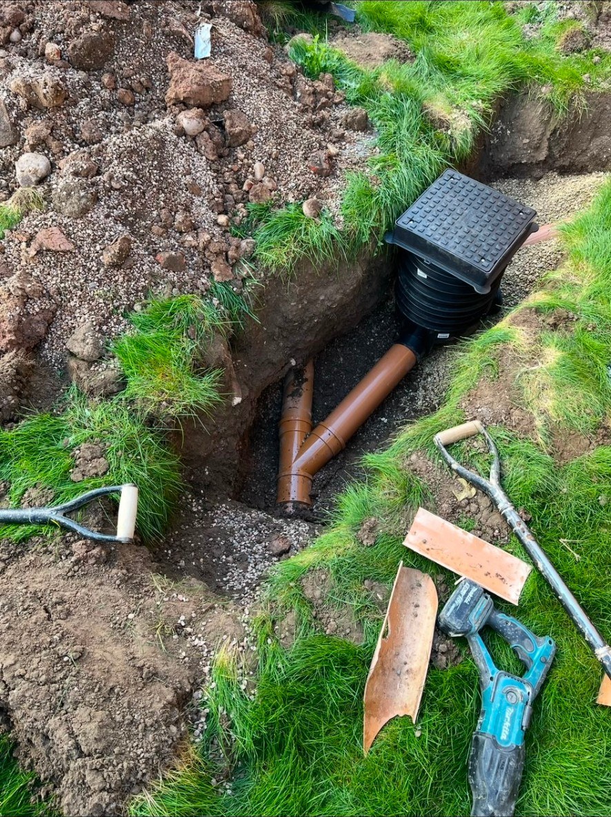 Installation of underground drainage pipes and inspection chamber in a garden trench.