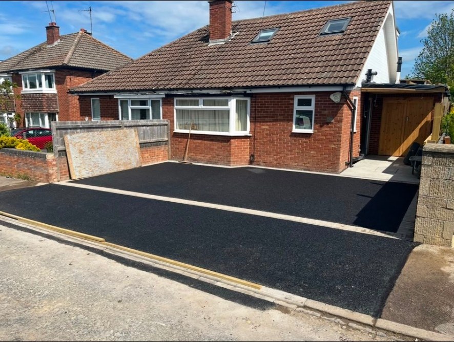 Newly laid black tarmac driveway for a red brick bungalow with stone paving border.