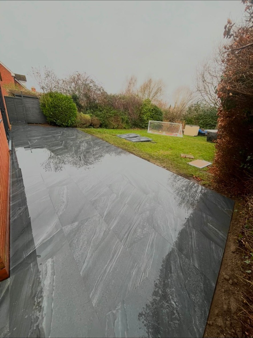 Large grey porcelain patio tiles with a textured grain finish in a residential garden.