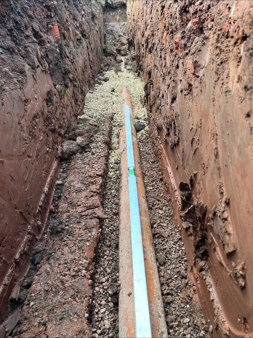 Professional drainage pipe installation in a deep ground trench with spirit level check.