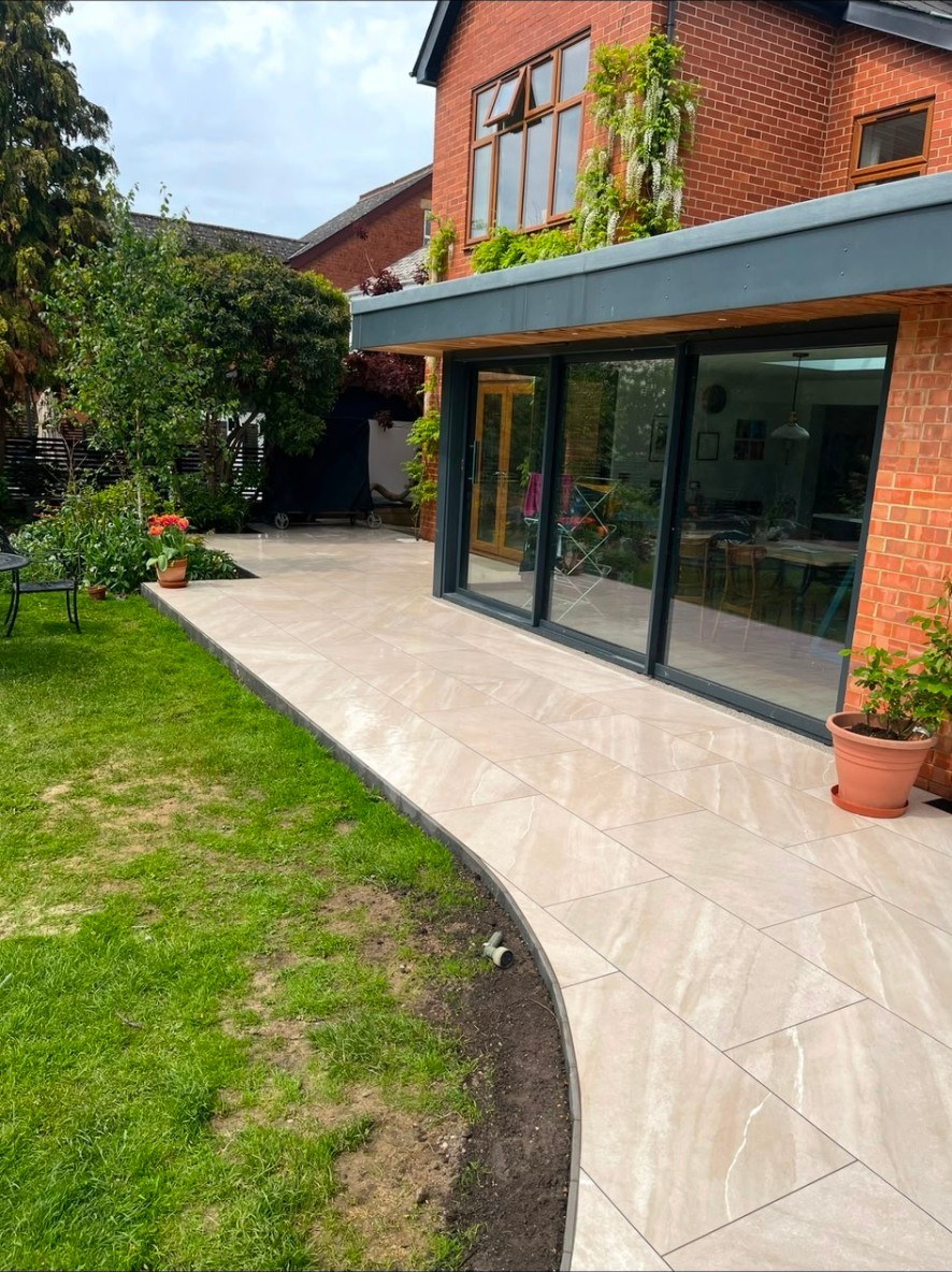 Contemporary beige porcelain tiled patio with curved edging outside a modern home extension.