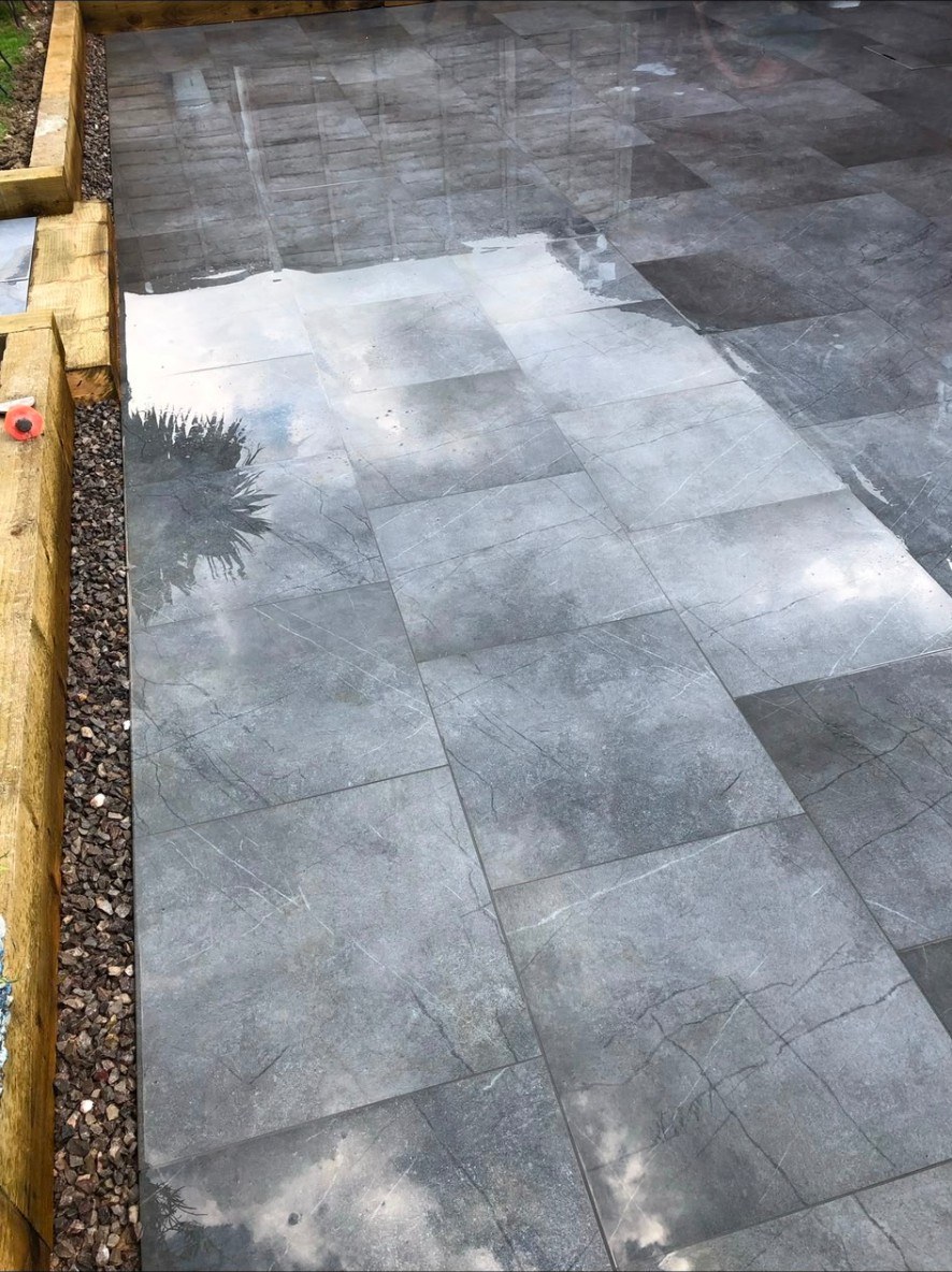Contemporary grey marble-effect porcelain patio tiles with timber sleeper borders and stone shingle.
