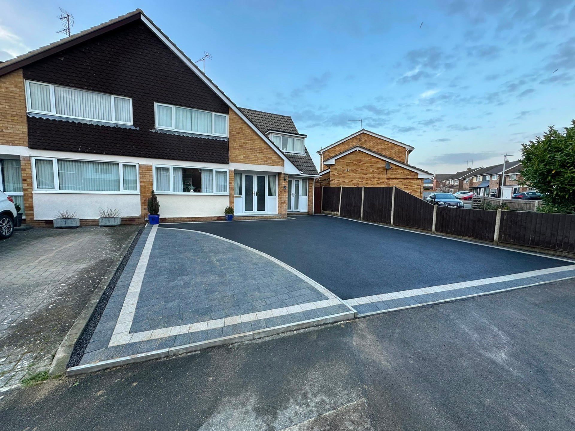Large dark grey asphalt driveway with block paved border and apron detail in front of a house.