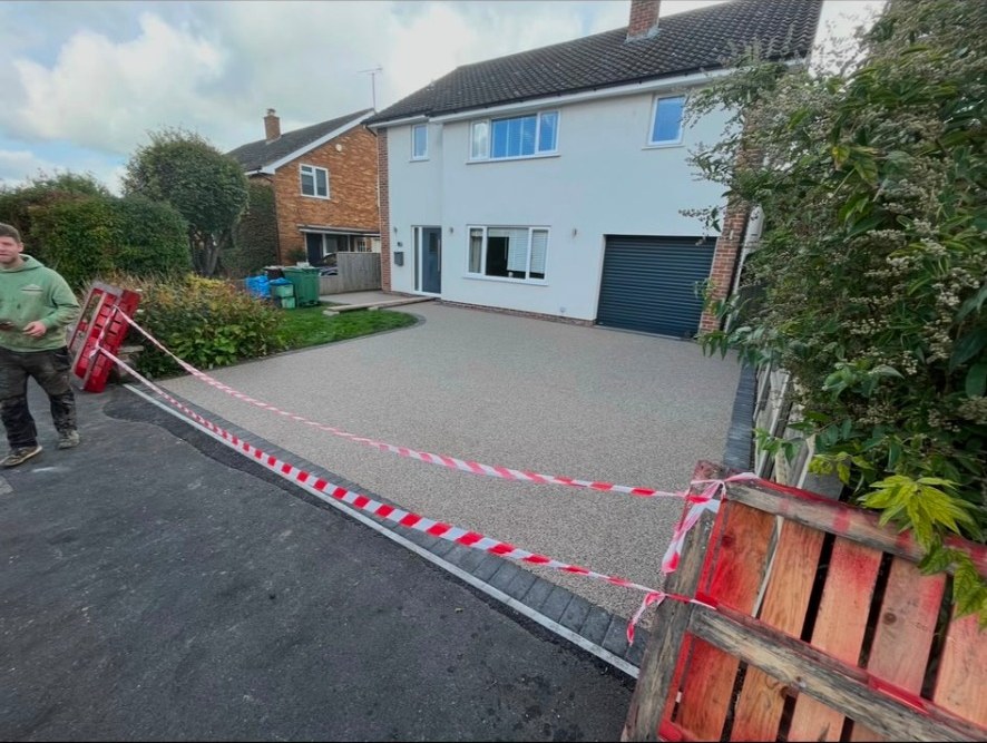 Newly installed resin-bound driveway with block paving border in front of a white detached house.