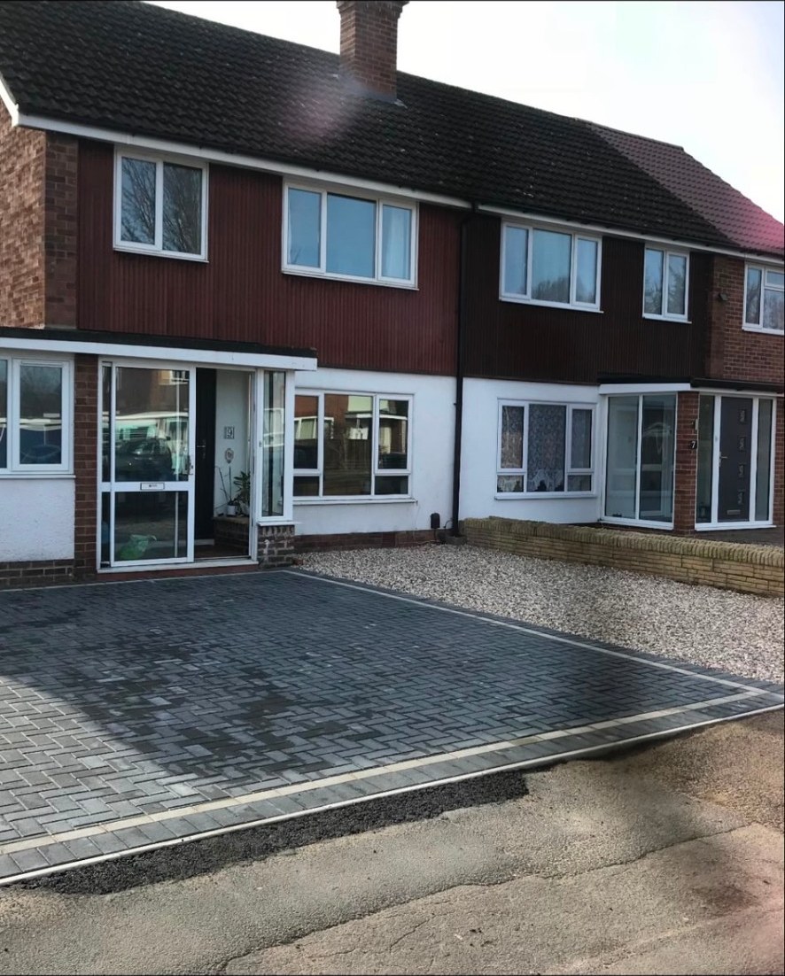 Newly installed charcoal block-paving driveway with decorative border and gravel area.