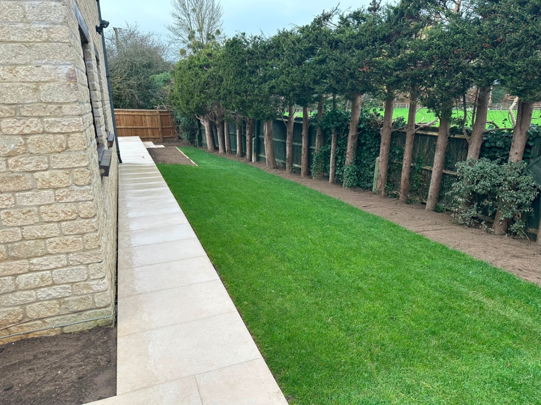 Newly turfed lawn with a smooth porcelain tile garden path alongside a stone house.
