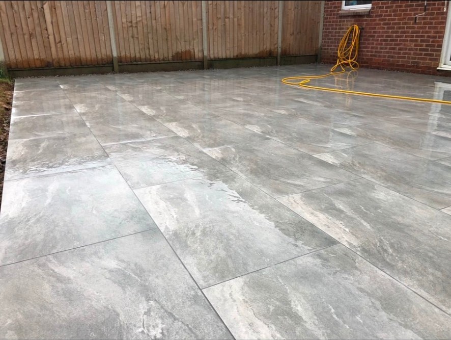 Newly installed grey porcelain patio tiles with a wet finish next to a timber fence.