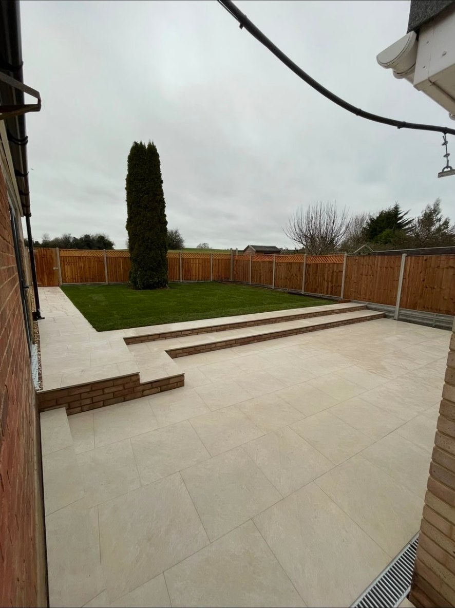 Tiered porcelain garden patio with brick retaining steps, new lawn, and timber fencing.