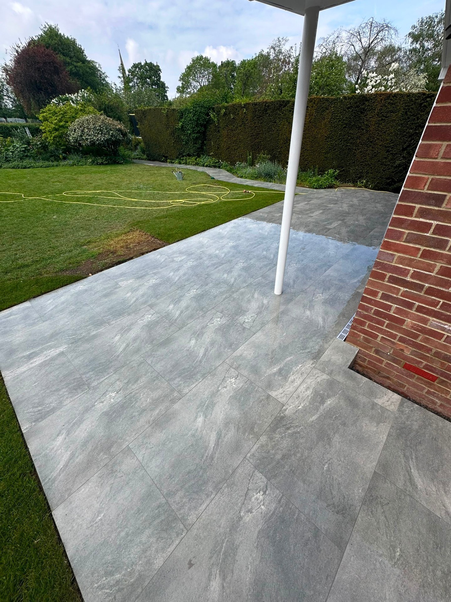 Contemporary grey porcelain patio tiles and garden lawn with hedge border.